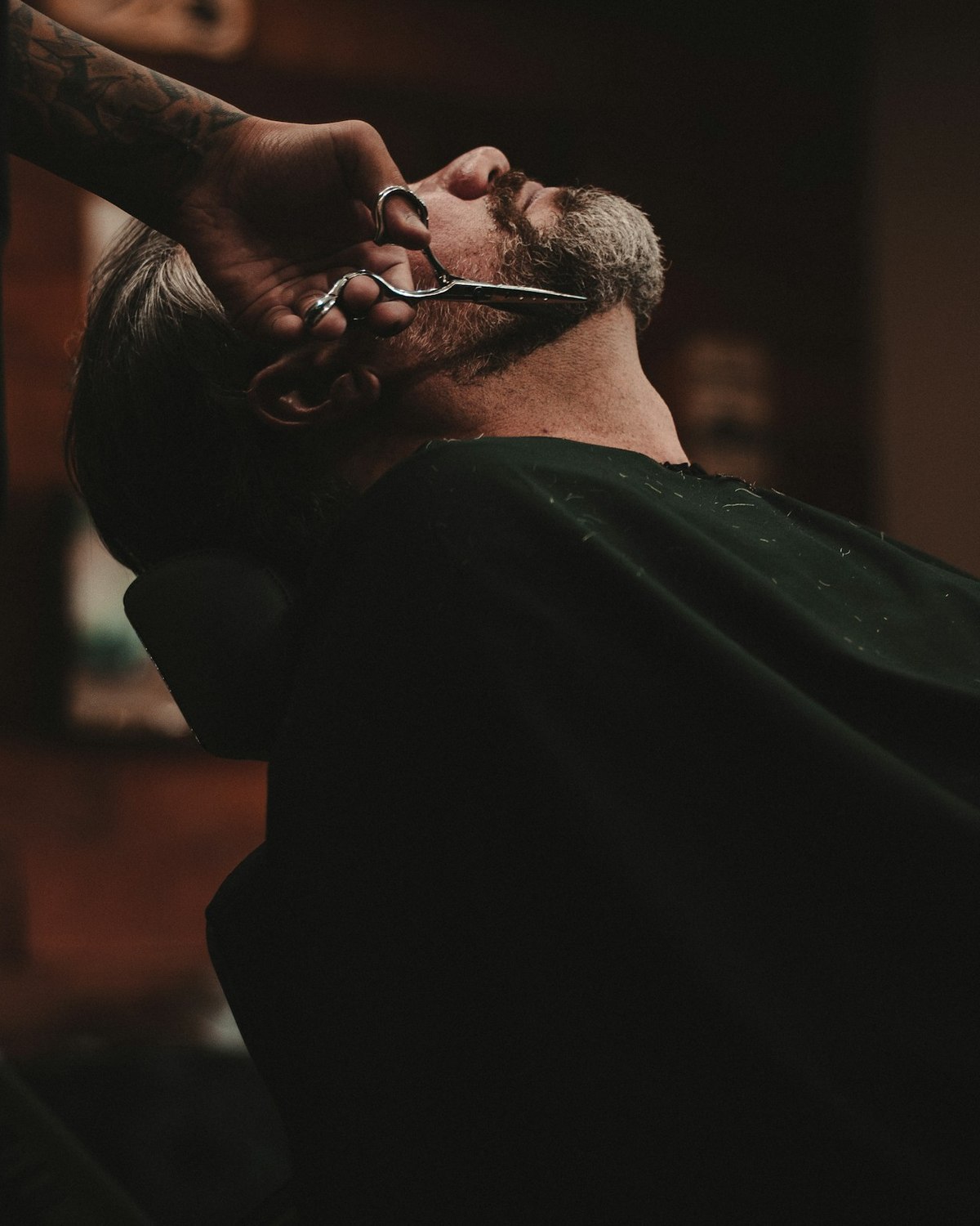 A barber working on a reclined customer, the shop dark behind them
